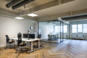Modern ingericht kantoor aan de De Ruijterkade met werkplekken, vergaderruimte van glas en houten visgraatvloer.